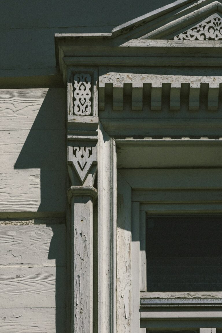 A person gently sanding an ornate wooden door frame inside a well-lit, early 20th-century home.