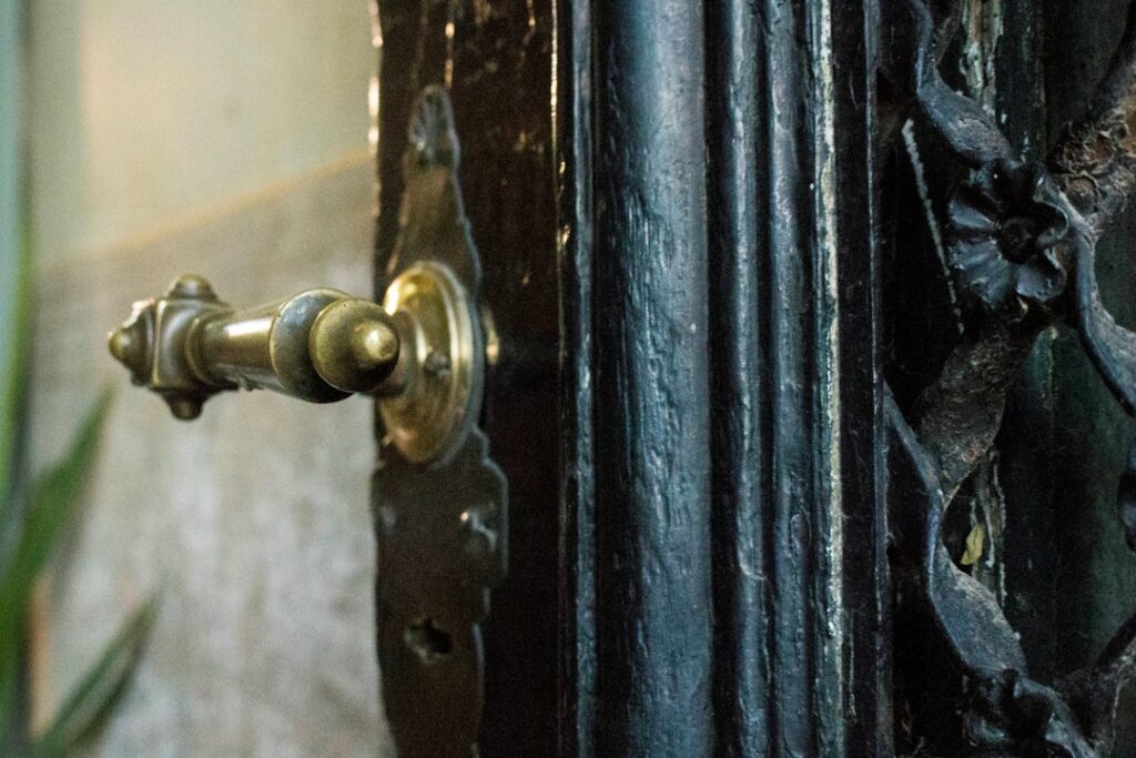 A homeowner compares brass knobs, iron hinges, and window latches beside an old wooden door.