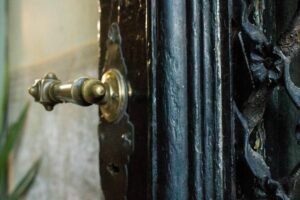 A homeowner compares brass knobs, iron hinges, and window latches beside an old wooden door.