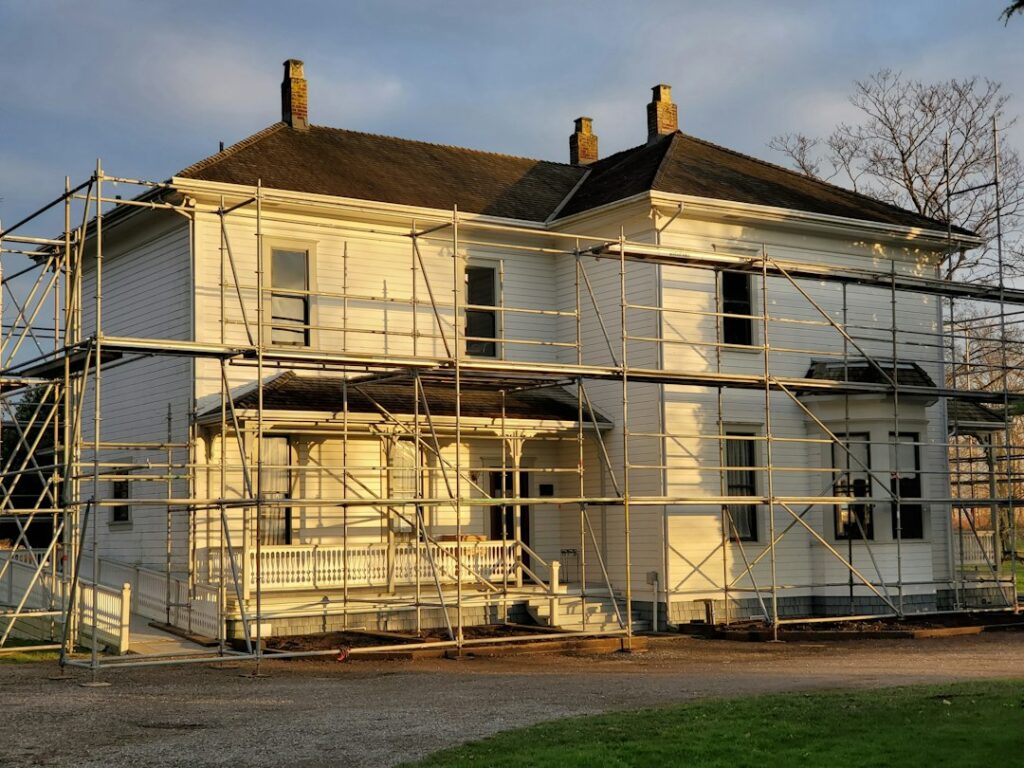 Homeowners examine old maps and photographs beside a historic house with visible stonework and original windows.
